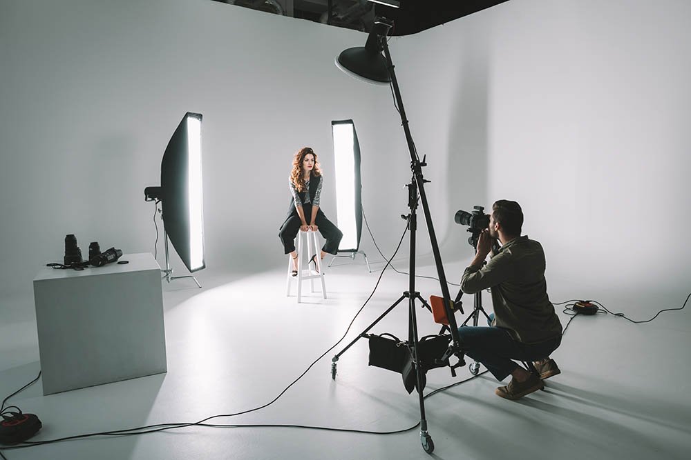 professional photographer and beautiful model on fashion shoot in photo studio with lighting equipment